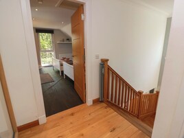 A hallway leading to a bedroom with a window, a wooden door, and a staircase with a wooden railing.