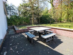 Eine Terrasse mit Picknicktisch und Bänken, umgeben von einer Ziegelmauer und viel Grün.