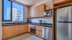 Cocina moderna con armarios de madera, electrodomésticos de acero inoxidable y un amplio ventanal con vistas a un edificio.