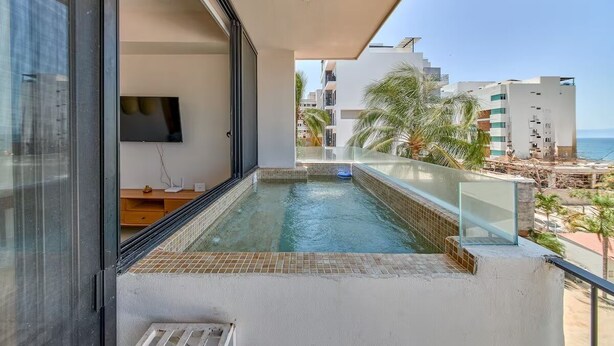 Un balcón con piscina, televisor y vistas a la playa y edificios.