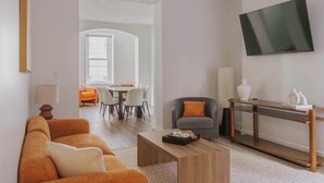 Una sala de estar moderna con sofá, mesa de centro, televisor y un área de comedor al fondo.