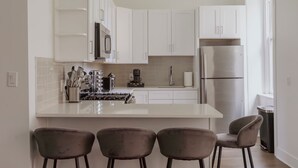 Una cocina moderna con armarios blancos, un refrigerador de acero inoxidable y una isla central con taburetes de bar.