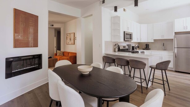 Una cocina moderna con armarios blancos, una isla central y un comedor con mesa oscura y sillas blancas.