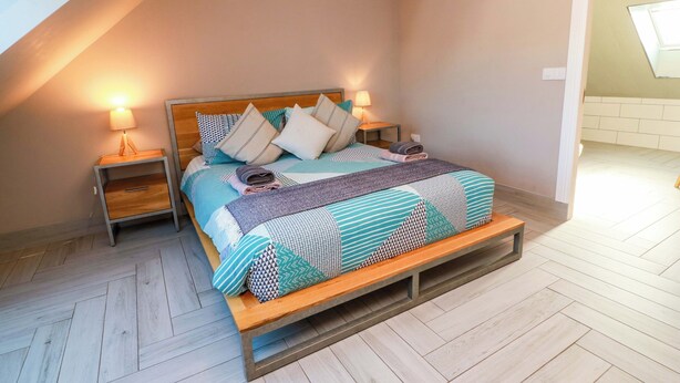 A bedroom with a wooden bed, two bedside tables, a bench, and a sloped ceiling. - Ledrishmore View (Alexandria)