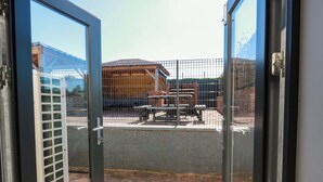 A view through a glass door of a building with a fenced outdoor area, a brick pathway, and a metal gate. - Ledrishmore View (Alexandria)