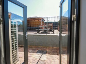 A view through a glass door of a building with a fenced outdoor area, a brick pathway, and a metal gate. - Ledrishmore View (Alexandria)