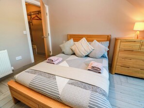 A neatly made bed with pillows and a blanket, a wooden bedside table, a wooden bench at the foot of the bed, and a wooden wardrobe. - Ledrishmore View (Alexandria)