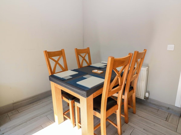 A corner room with a wooden table and chairs, a radiator, and a light switch on the wall. - Ledrishmore View (Alexandria)