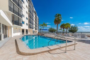 A swimming pool with lounge chairs and palm trees, adjacent to a building with balconies. - Carlos Pointe #523-shelloway (Fort Myers Beach)
