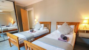 Two wooden beds with white linens, a wooden headboard, and a bedside table with a lamp. - Ballaganlea (Alexandria)