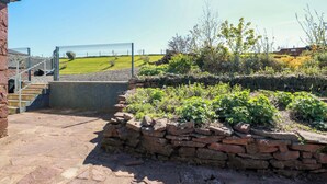 A stone staircase leading to a gated entrance, a stone wall with plants, and a clear blue sky. - Ballaganlea (Alexandria)