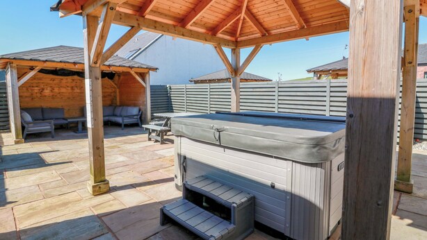 A hot tub under a wooden pergola in a backyard with a patio area and a covered seating space. - Ballaganlea (Alexandria)