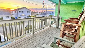 Terraza de madera con barandilla que da a una calle residencial y un atardecer.