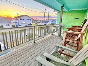 Eine Holzterrasse mit Geländer, die auf eine Wohnstraße und einen Sonnenuntergang blickt.