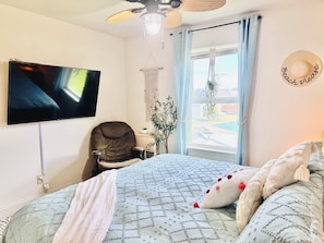 A bedroom with a bed, a chair, a television, and a window with curtains.