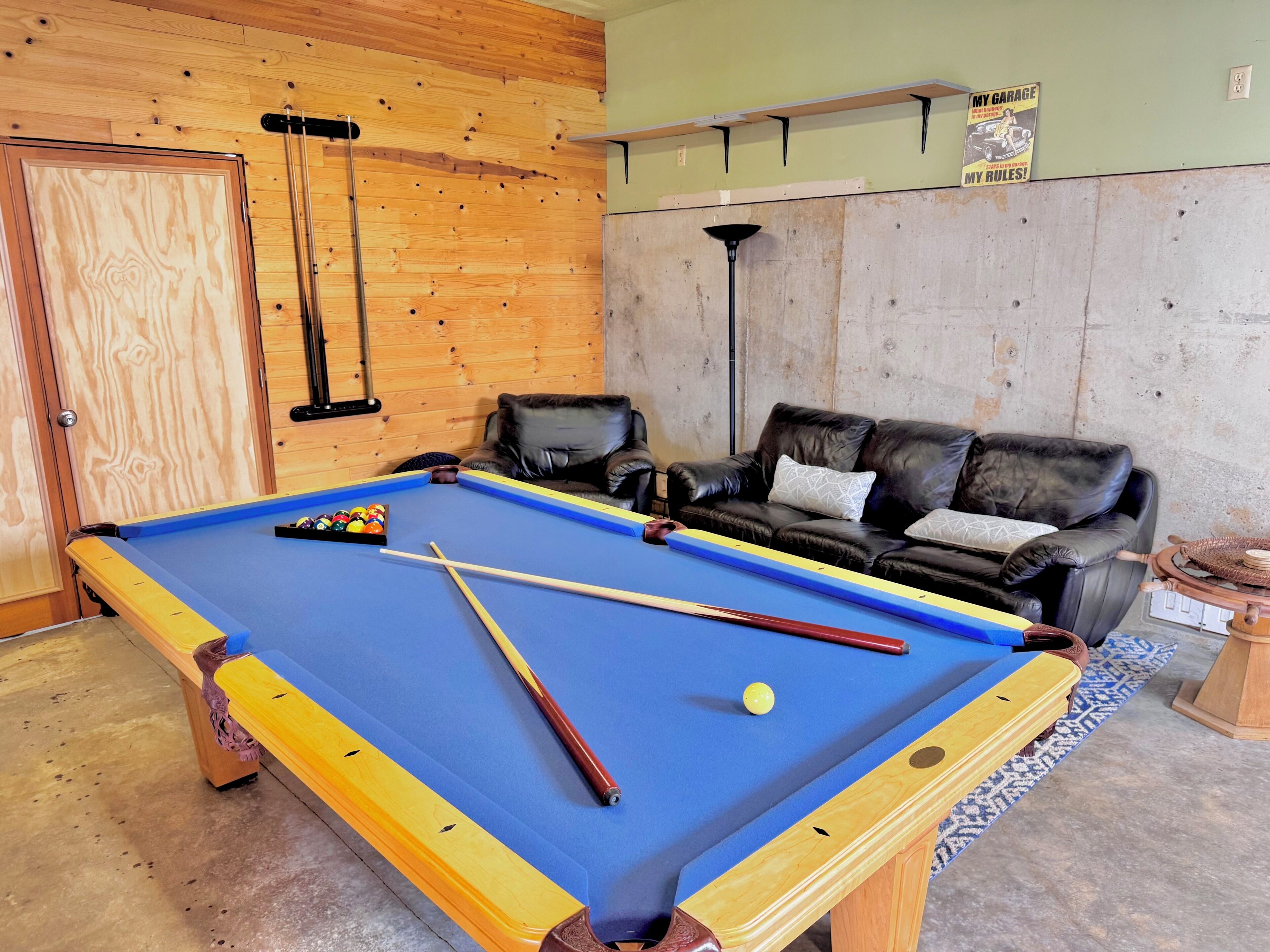 Une table de billard avec queues et billes, un canapé en cuir et une lampe fixée au mur.