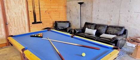 A pool table with cues and balls, a leather sofa, and a wall-mounted lamp.