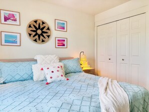 Ein Schlafzimmer mit einem Bett, Kissen, einer Lampe und gerahmten Bildern an der Wand.