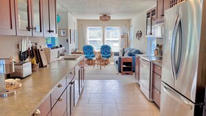 Una cocina moderna con una isla central, un comedor con sillas azules y un refrigerador grande.