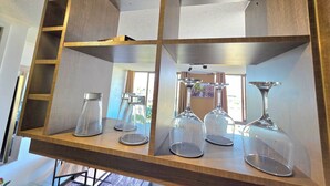 A wooden shelf with glassware, including wine glasses and a decanter, in a room with a window and a painting. - Hermoso Departamento Estación Central (Santiago)