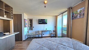 A hotel room with a bed, a desk with a chair, a TV, and a large window with a city view. - Hermoso Departamento Estación Central (Santiago)