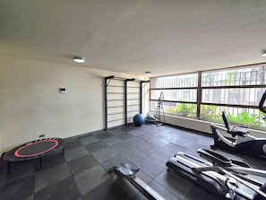 A gym with exercise equipment, a trampoline, and a window with a view of greenery.