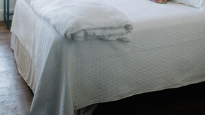 Una cama bien tendida con sábanas blancas, una mesita de noche con lámpara y un cuadro en la pared.