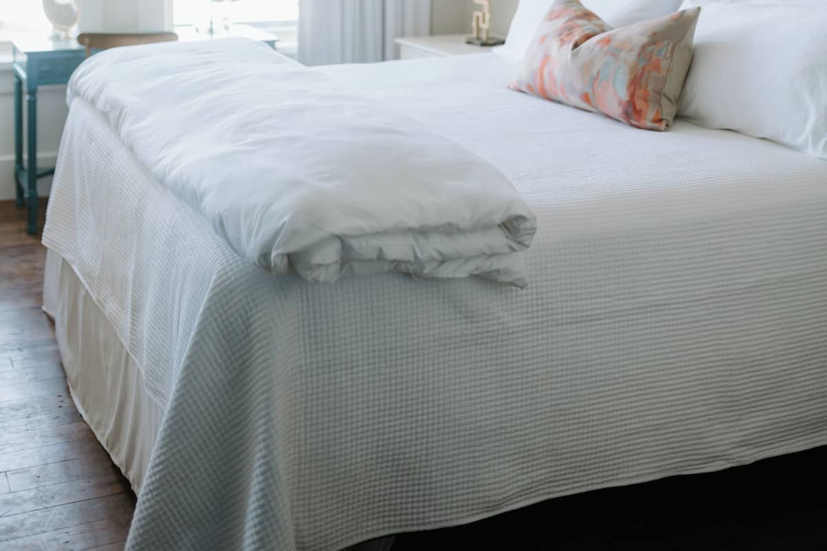 A neatly made bed with white linens, a bedside table with a lamp, and a painting on the wall.