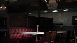 Un restaurante tenuemente iluminado con una cabina tapizada en rojo, mesas blancas y sillas de madera oscura.
