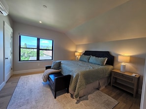 Quarto com uma janela grande, uma cama, uma cadeira, uma mesa de cabeceira e um abajur.