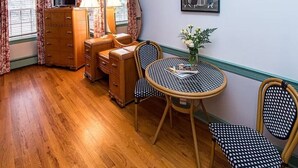 A room with a wooden dresser, two chairs, a round table, a mirror, and a framed picture on the wall.