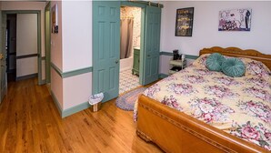 A bedroom with a wooden bed, a nightstand, a green door, a bathroom with a bathtub, and a wall with a poster.