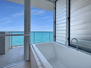Un baño moderno con bañera, ducha y un balcón de cristal con vistas al océano.