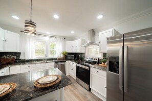 A modern kitchen with stainless steel appliances, white cabinetry, and a large island with a marble countertop. - Spacious 3BR Retreat~ Weddings, Crews & Families (Little Rock)