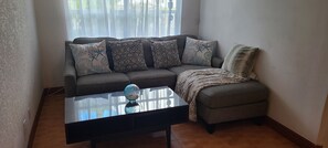 A living room with a sofa, a glass coffee table, and a blanket.