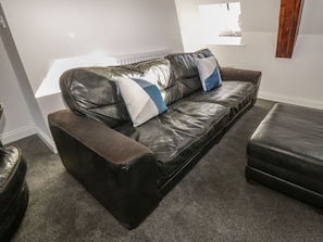 Un sofá de cuero negro con un reposapiés a juego y un banco acolchado, ubicado en una habitación con piso alfombrado y una ventana con persianas.