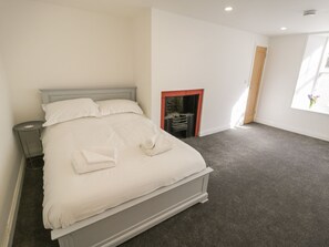 A bedroom with a bed, a nightstand, a fireplace, and a window. - 47 Baxtergate (Whitby)