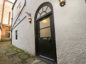 A white building with a black door marked with the number 47, a small window, and a wall-mounted light fixture. - 47 Baxtergate (Whitby)