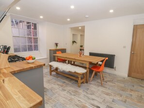 A modern kitchen with a wooden table, orange chairs, a white bench, and a window with a view. - 47 Baxtergate (Whitby)