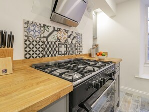 A kitchen with a gas stove, oven, and a decorative backsplash. - 47 Baxtergate (Whitby)