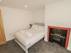 A bedroom with a bed, a wooden door, a fireplace, and a vase with flowers. - 47 Baxtergate (Whitby)