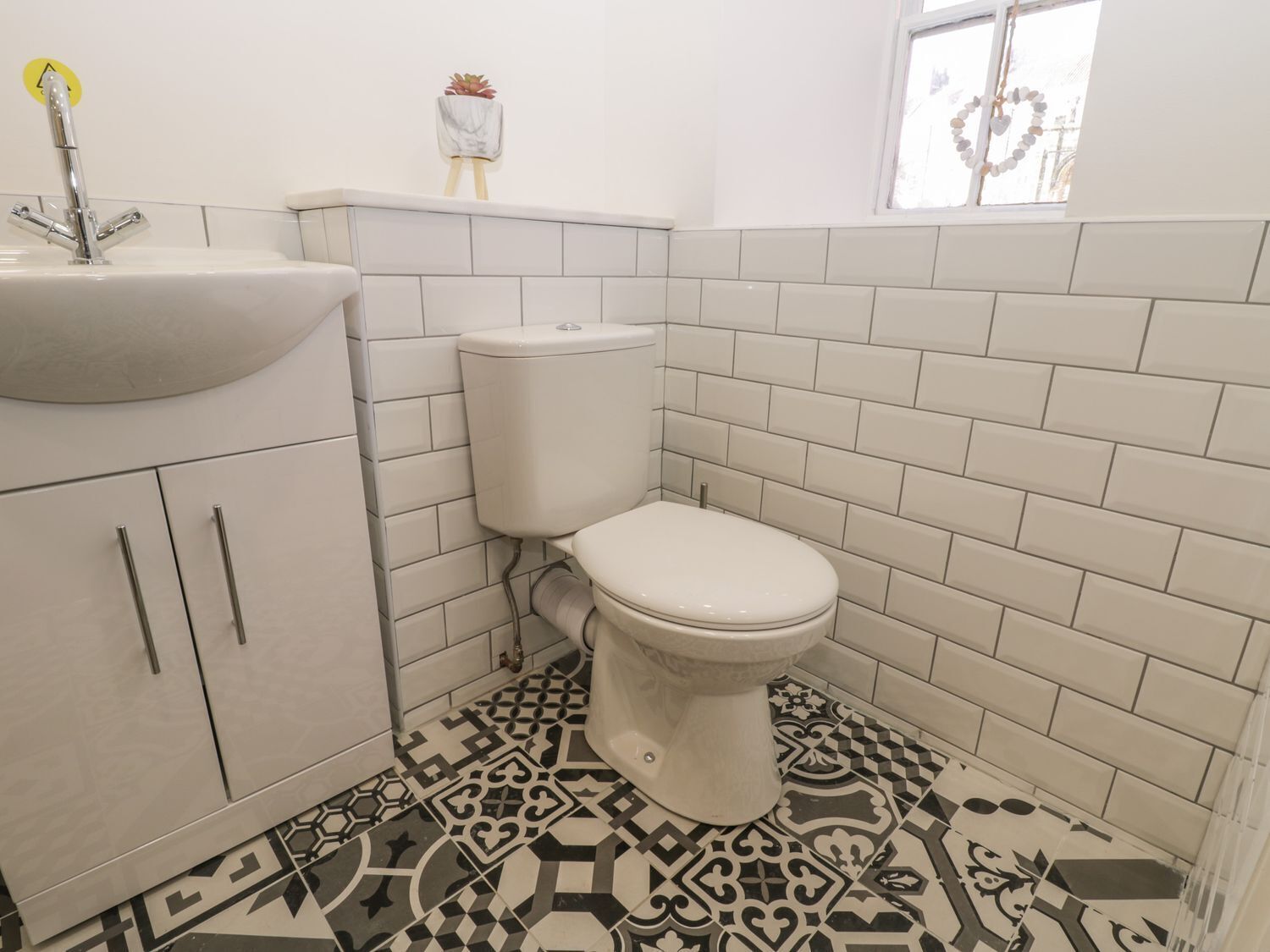 Un baño con inodoro blanco, lavamanos y baldosas de suelo estampadas.