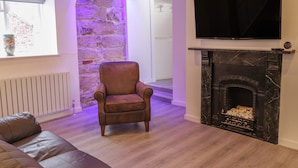 Un salon avec un mur d’accent en pierre, une cheminée, un canapé en cuir et un téléviseur fixé au-dessus de la cheminée.