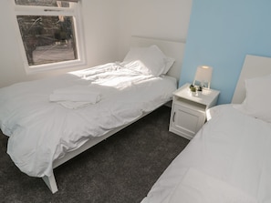 Ein Schlafzimmer mit einem Bett, einem Nachttisch mit Lampe und einem Fenster.