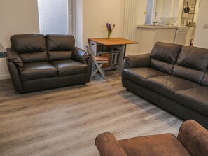 A living room with two brown leather sofas, a wooden coffee table, and a small kitchen area in the background. - 47A Baxtergate (Whitby)