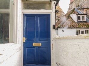 A blue door with a brass knocker, a white wall, and a window with a white frame. - 47A Baxtergate (Whitby)