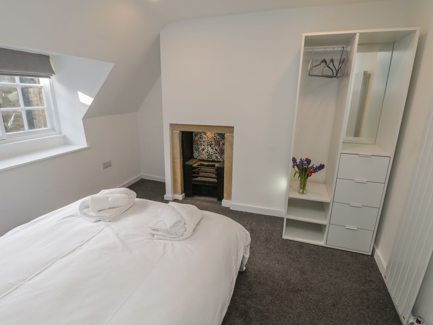 A bedroom with a bed, a wardrobe, a mirror, a fireplace, and a window.