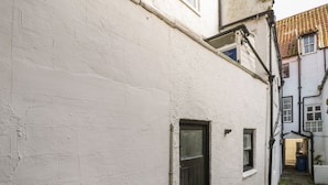Une ruelle étroite avec un bâtiment blanc, une porte noire et une fenêtre.