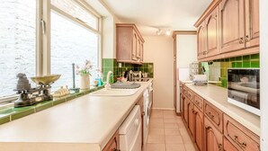 A kitchen with wooden cabinets, a sink, a stove, and a window. - The Anchorage (Whitby)