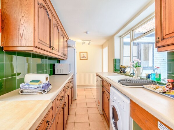 A kitchen with wooden cabinets, a microwave, a washing machine, and a window with a view. - The Anchorage (Whitby)
